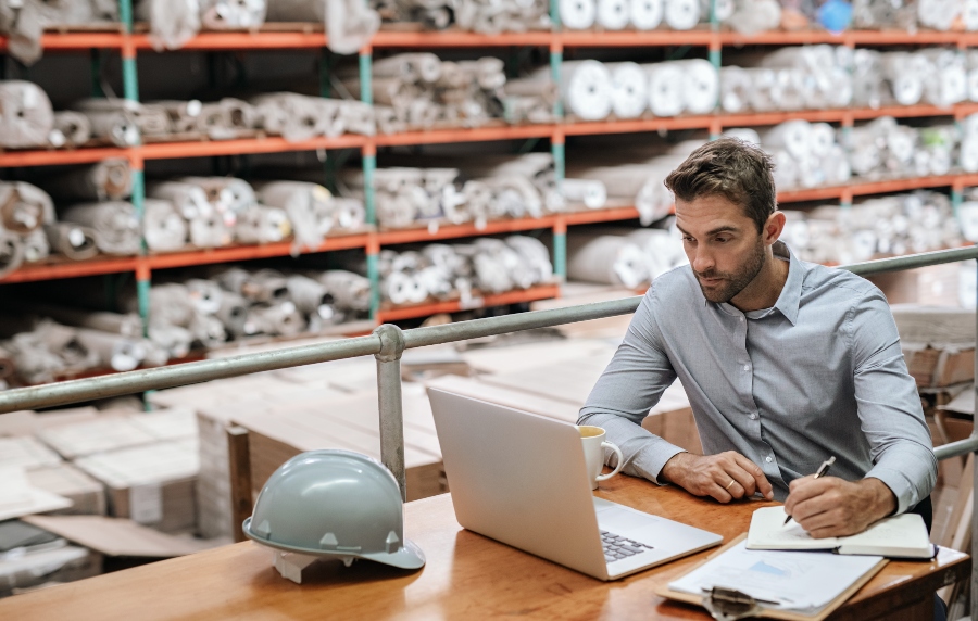 Bei bereits vorhandenem Ladengeschäft ist der Sprung ins Online-Business etwas leichter Junger Mann sitzt im Lager am Laptop - Onlineshop gründen