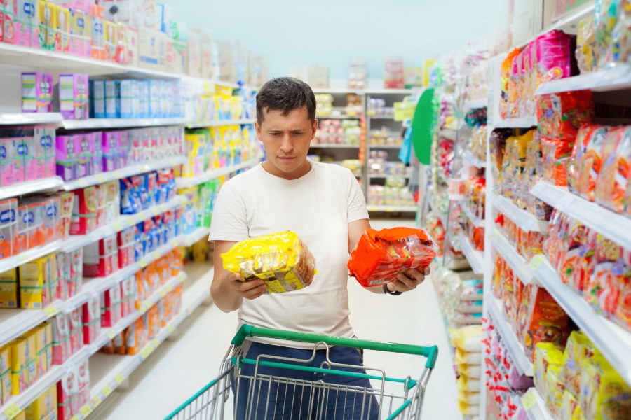 Mann vergleicht gleichartige Produkte im Supermarkt