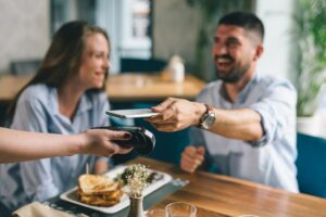 Junges Paar bezahlt in einem Restaurant mit Handy - so entsteht Umsatz