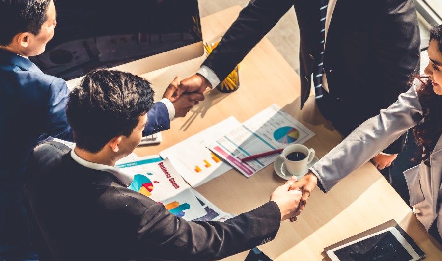 Für Joint Ventures gilt, was für alle Partnerschaften gilt: beide profitieren Symbolbild, 4 Menschen in Anzügen geben sich die Hand als Zeichen für Kooperation - Welche Vorteile bietet ein Joint Venture?